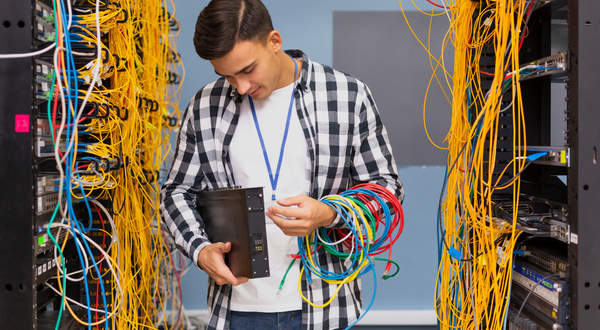 Man in plaid shirt holding black network switch with ethernet cables
