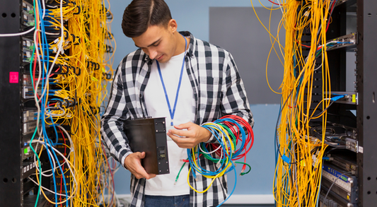 Man in plaid shirt holding black network switch with ethernet cables