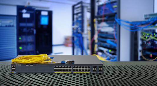 Gray network switch with coiled yellow fiber optic cable on top