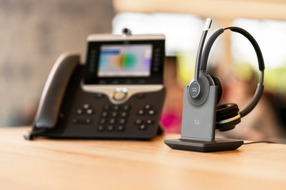Gray cisco cp-hs-wl-562-s-eu wireless dual-ear headset with black headband resting on charging stand